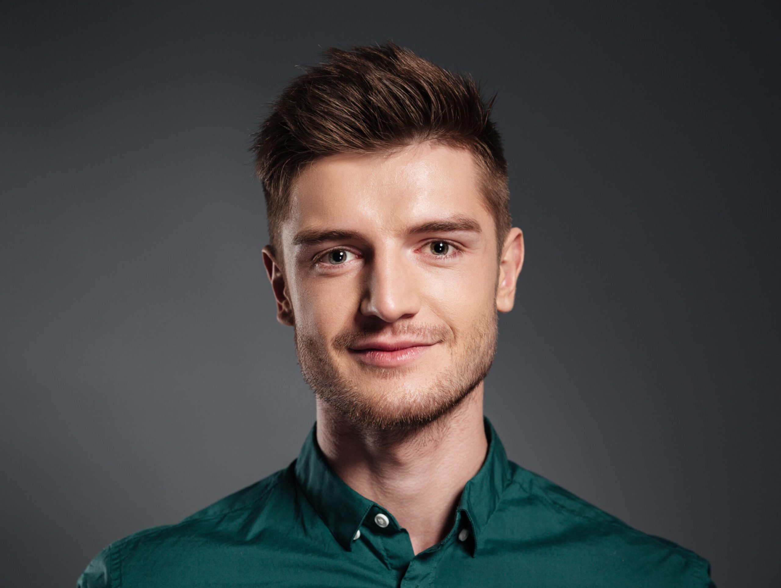Photo of cheerful young man posing isolated over grey background. Looking at camera.